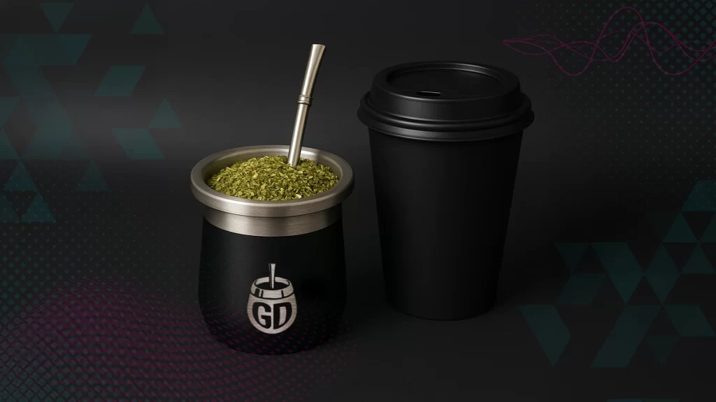 Silver and black mug with yerba mate floating on top and a bombia sticking, out slightly in front of a black to-go cup with lid.